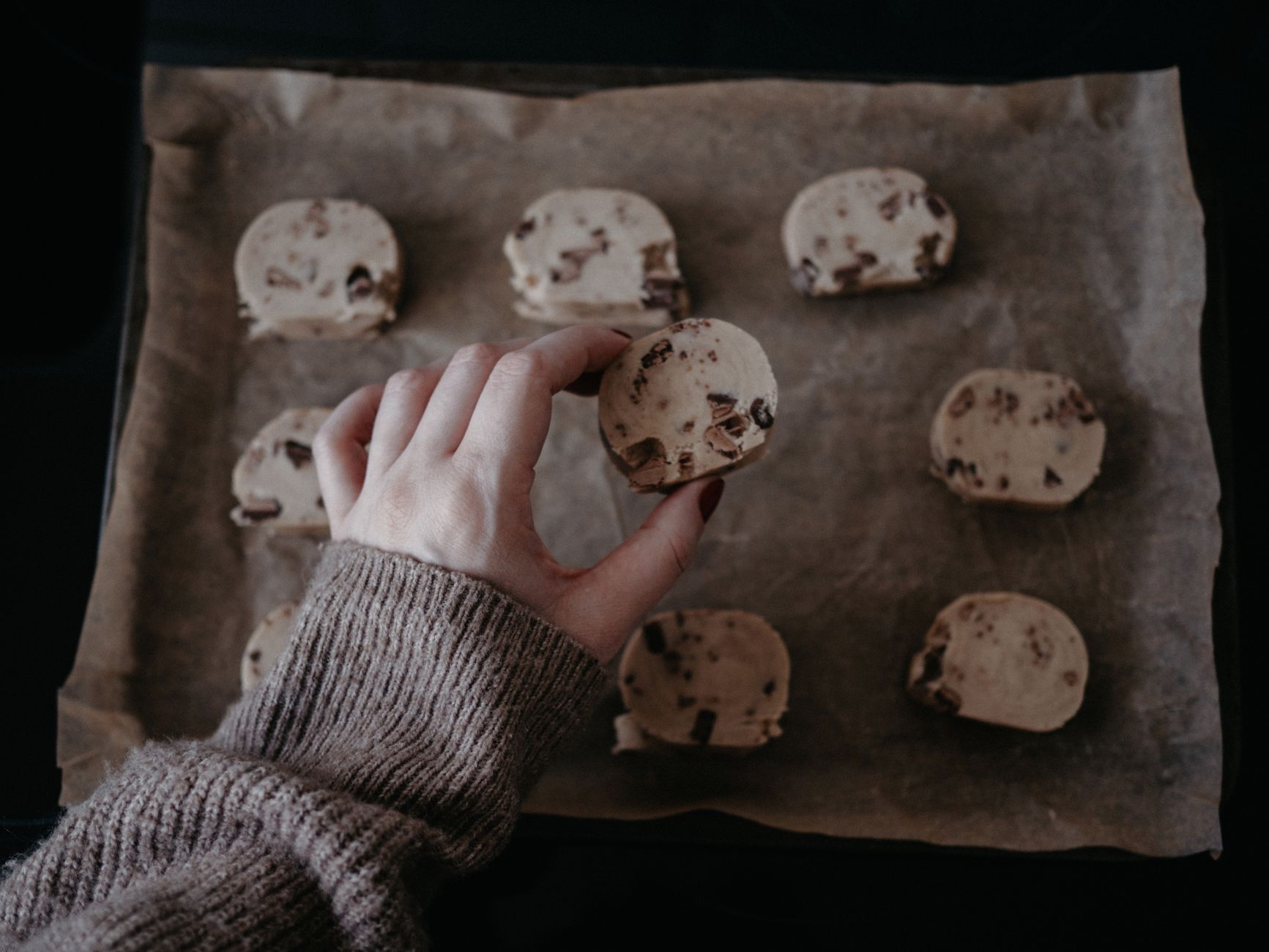 A hand placing chocolate chip cookie dough onto a lined baking tray