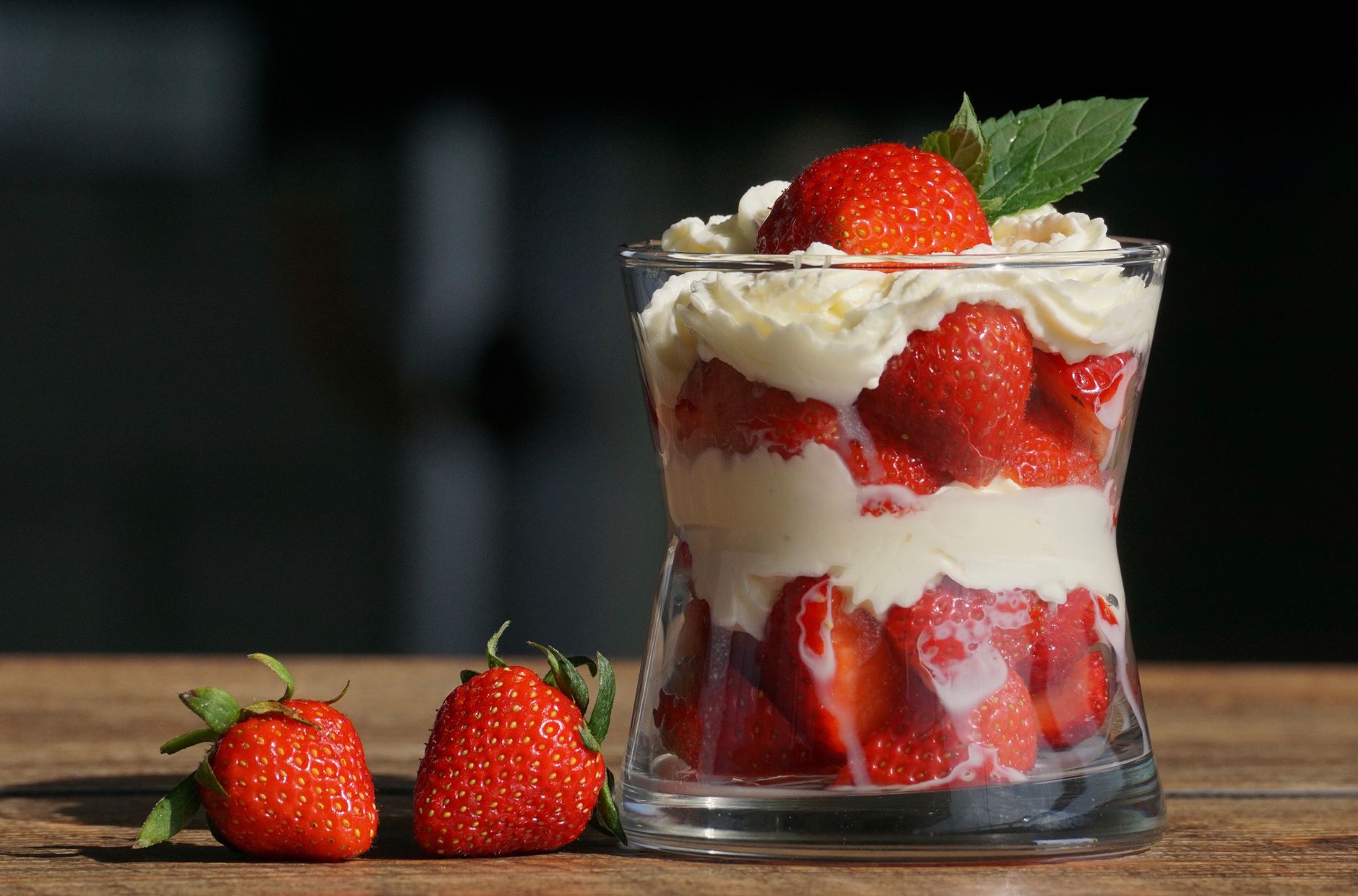 Layers of strawberries and cream in a glass with fresh strawberries beside it