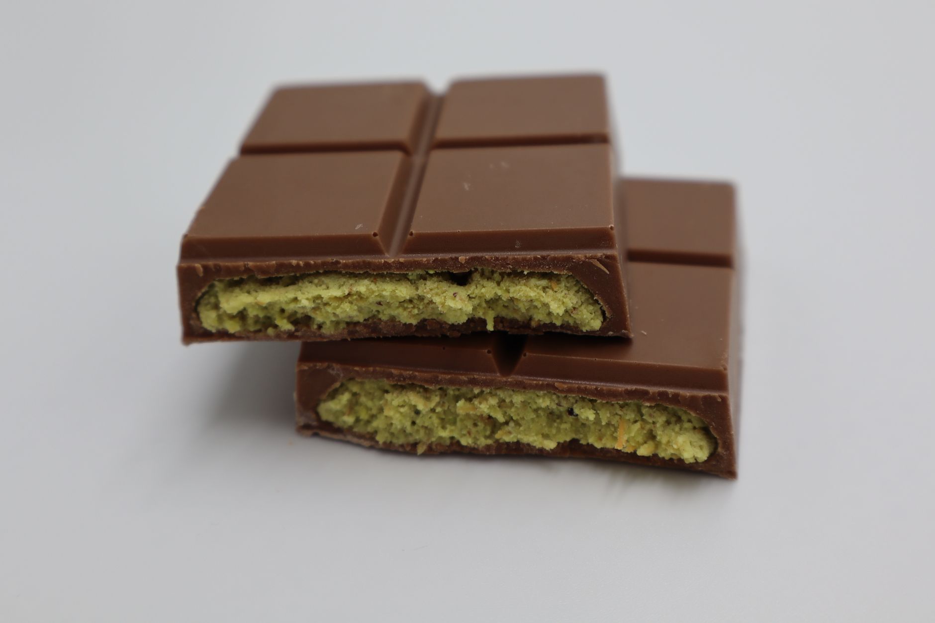 A milk chocolate bar broken open to show a green pistachio filling