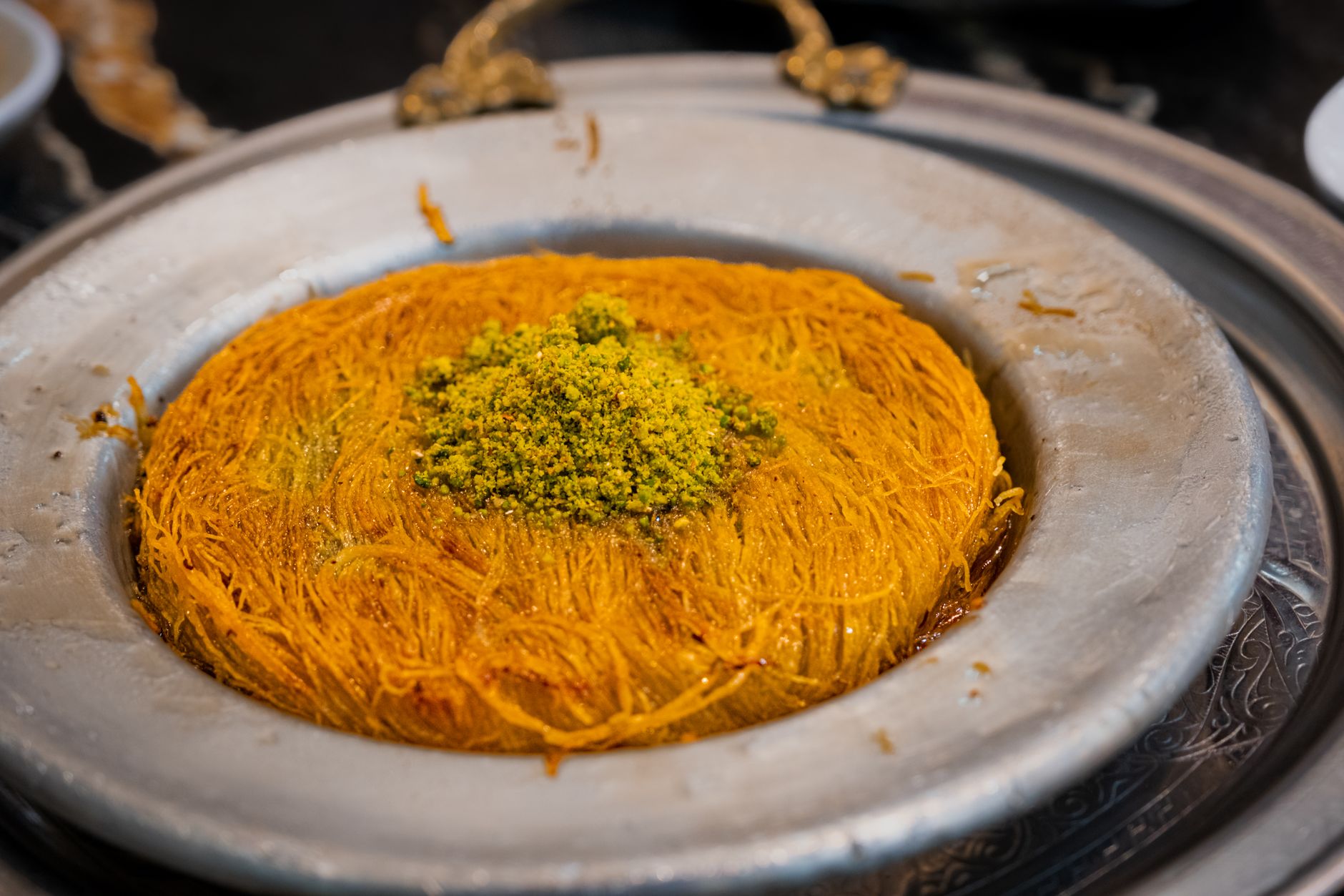 A tray of golden kunafa topped with ground pistachio
