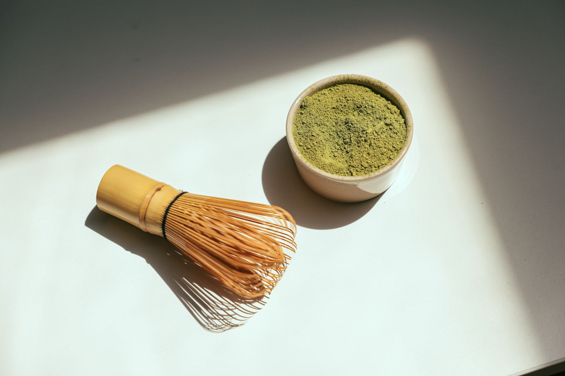 Matcha powder in a bowl beside a bamboo whisk in bright sunlight