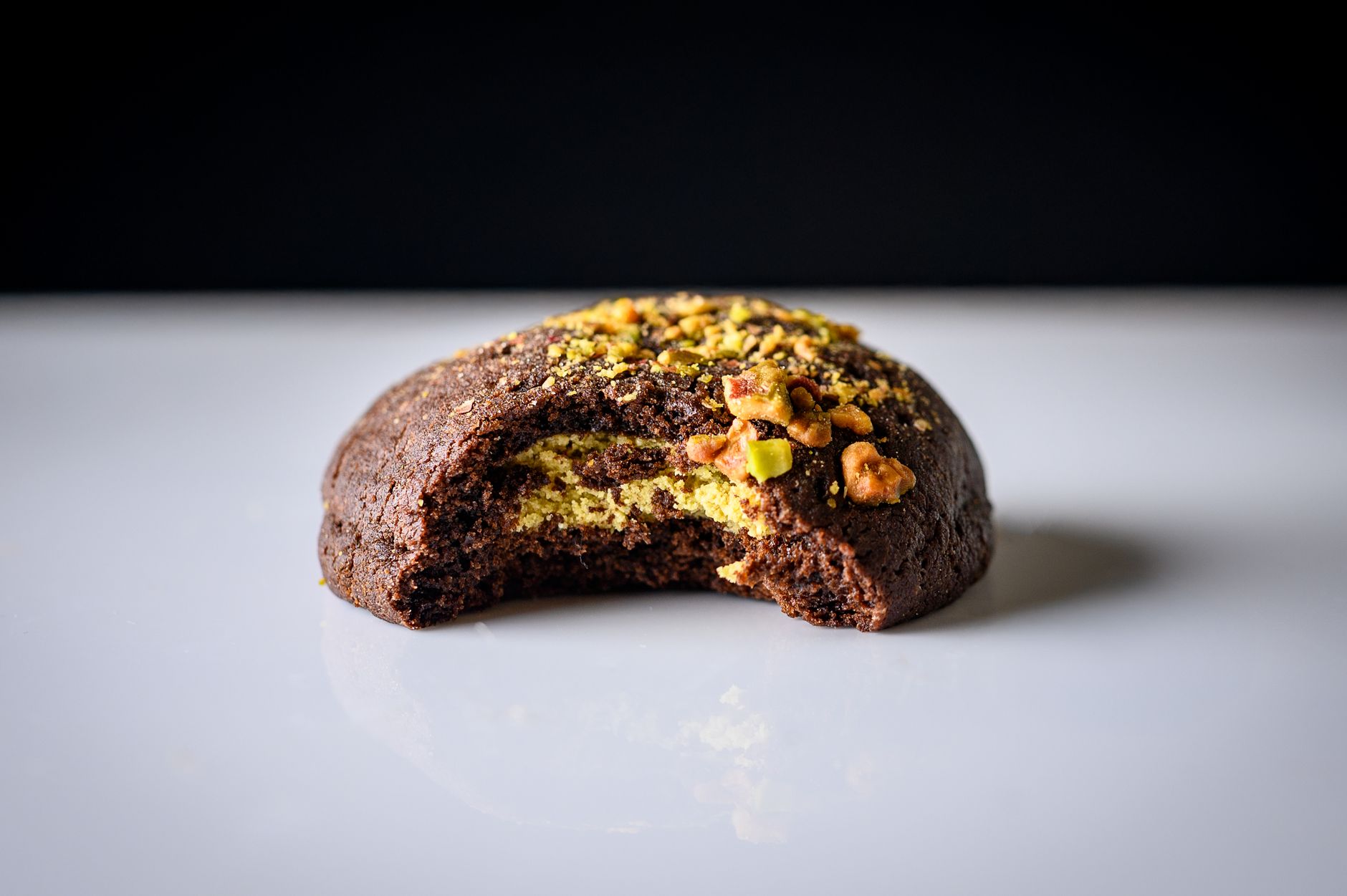 A chocolate cookie with a bite taken out showing a green pistachio filling