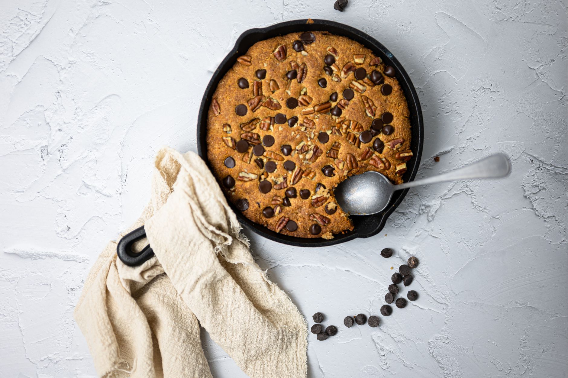 A chocolate chip and pecan cookie baked in a cast iron skillet with a spoon