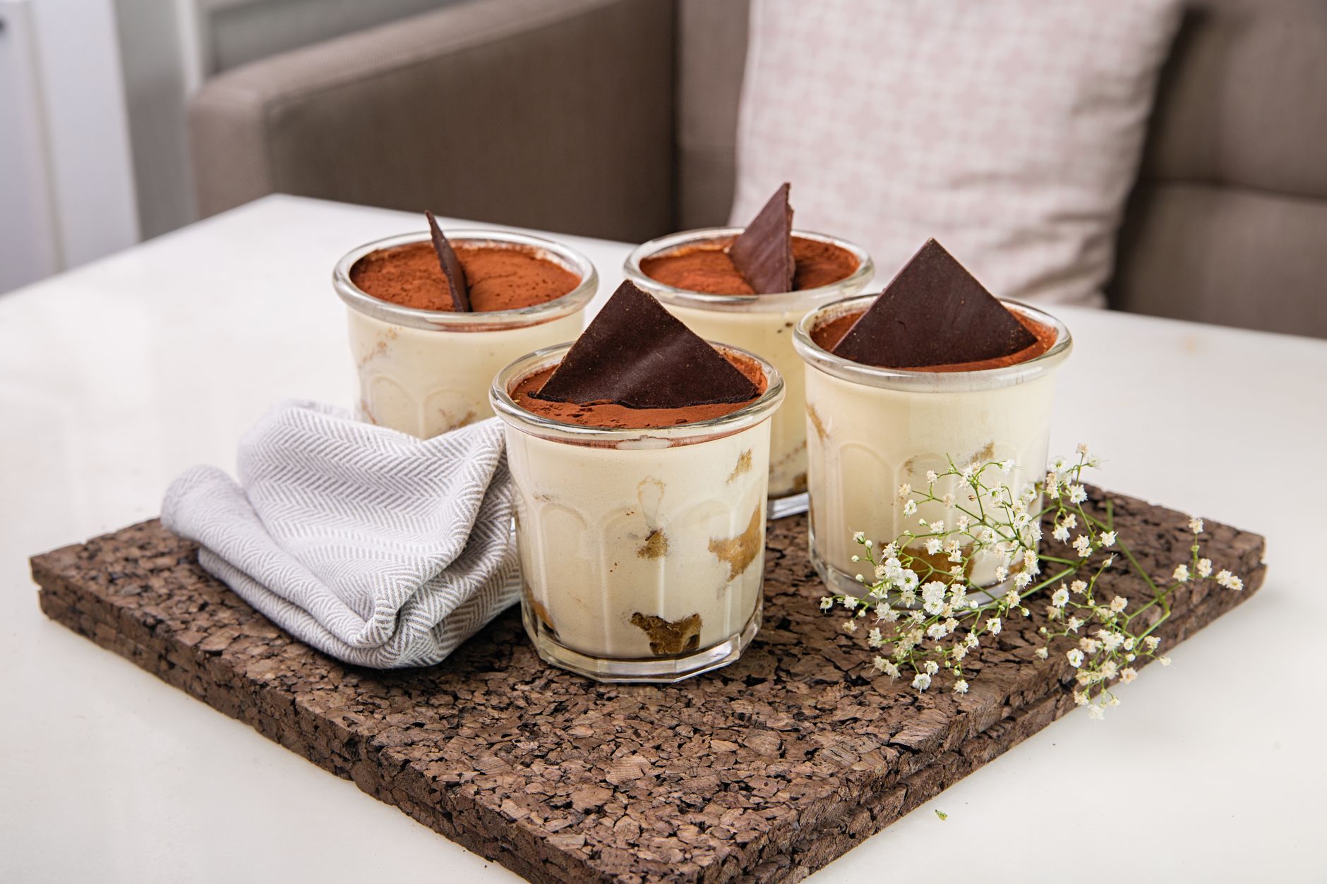 Four tiramisu desserts in glass cups dusted with cocoa on a board